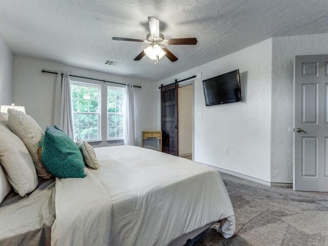 bedroom with carpet, a textured ceiling, a barn door, and ceiling fan