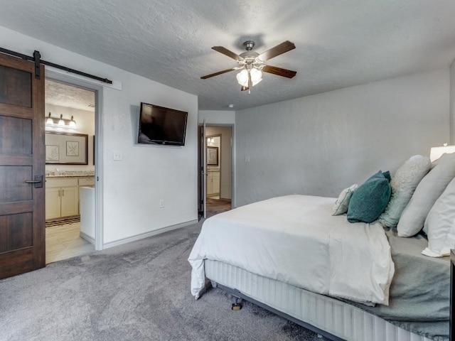 carpeted bedroom with a textured ceiling, ceiling fan, a barn door, and ensuite bathroom