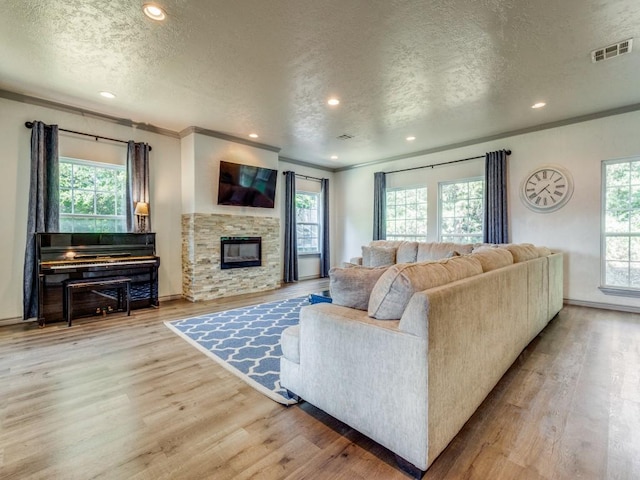 living room with a stone fireplace, crown molding, light hardwood / wood-style flooring, and a textured ceiling