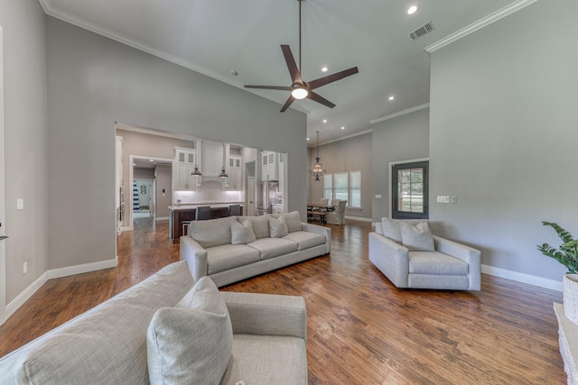 living room with crown molding, a towering ceiling, dark hardwood / wood-style floors, and ceiling fan