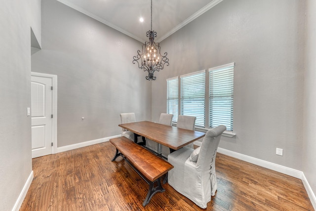 dining room with a high ceiling, wood-type flooring, a notable chandelier, and crown molding