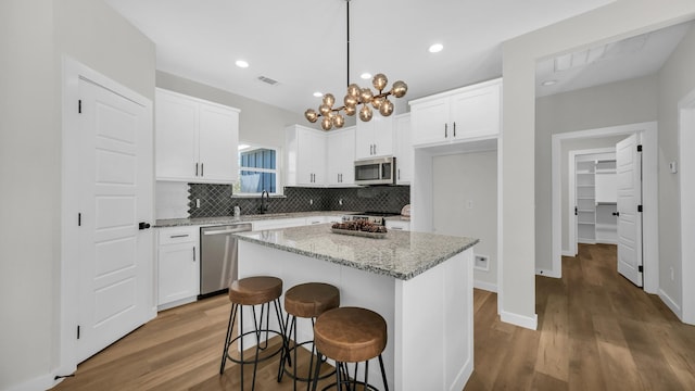 kitchen featuring light stone counters, stainless steel appliances, a center island, white cabinetry, and hanging light fixtures