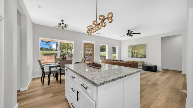 kitchen with ceiling fan with notable chandelier, hanging light fixtures, light stone countertops, a kitchen island, and white cabinetry