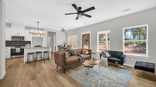 living room with ceiling fan with notable chandelier and light wood-type flooring