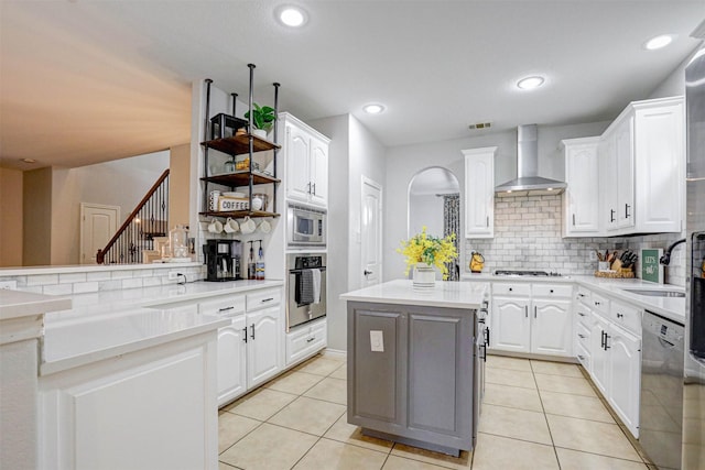 kitchen with a center island, backsplash, wall chimney range hood, appliances with stainless steel finishes, and white cabinetry