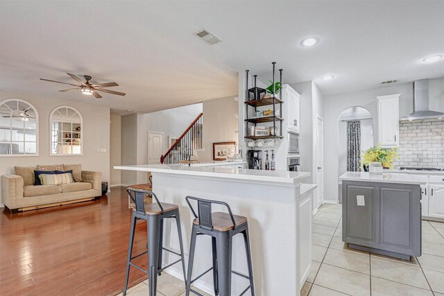 kitchen featuring white cabinetry, a center island, wall chimney range hood, decorative backsplash, and appliances with stainless steel finishes