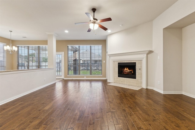 unfurnished living room with a tiled fireplace, ceiling fan with notable chandelier, and dark hardwood / wood-style floors