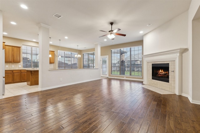 unfurnished living room with ceiling fan with notable chandelier, light hardwood / wood-style flooring, a tile fireplace, and plenty of natural light