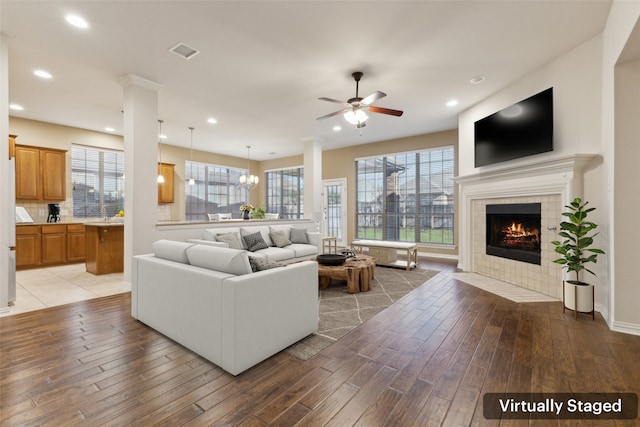 living room with ceiling fan with notable chandelier, a tiled fireplace, and hardwood / wood-style floors