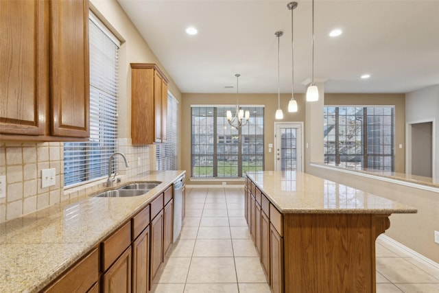 kitchen with sink, a center island, stainless steel dishwasher, pendant lighting, and light stone countertops