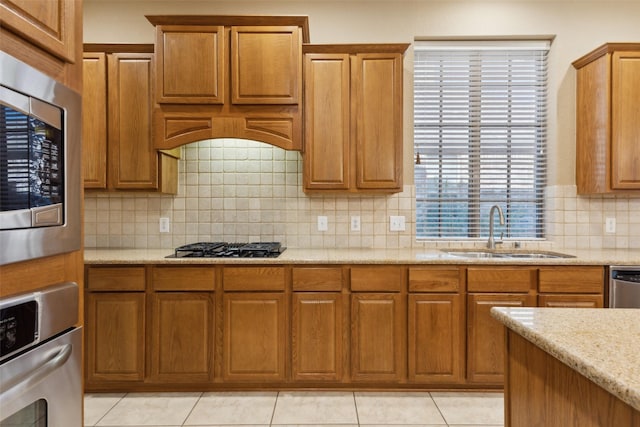 kitchen featuring sink, light tile patterned floors, appliances with stainless steel finishes, backsplash, and light stone countertops