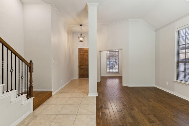 entryway featuring vaulted ceiling, a chandelier, ornamental molding, light hardwood / wood-style floors, and decorative columns