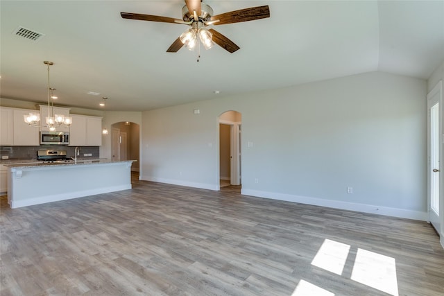 interior space with stove, backsplash, white cabinets, an island with sink, and decorative light fixtures