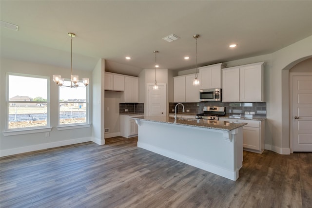 kitchen featuring appliances with stainless steel finishes, dark wood-type flooring, a center island with sink, stone counters, and white cabinets