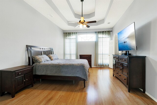 bedroom with a raised ceiling, ceiling fan, and light hardwood / wood-style floors