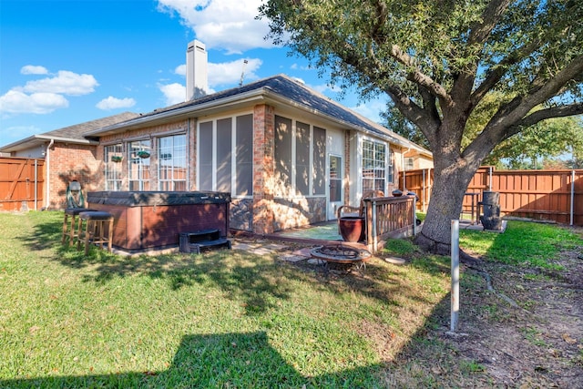 rear view of property featuring a lawn, a hot tub, and an outdoor fire pit