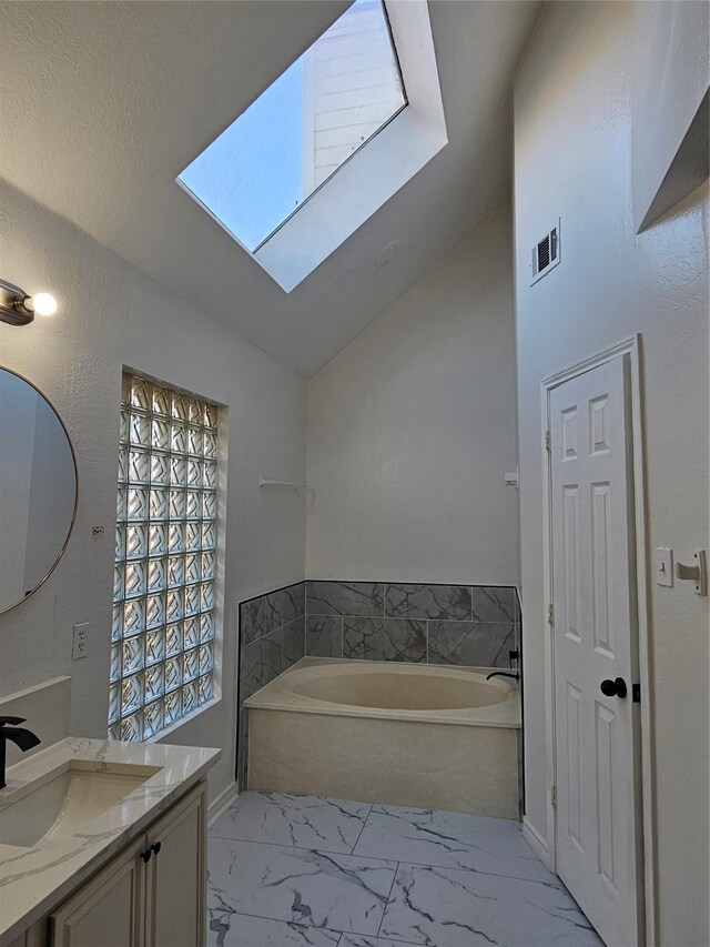 bathroom with vanity, vaulted ceiling with skylight, and a bathing tub