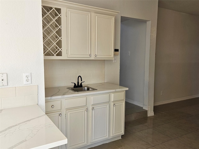 kitchen with light stone countertops, tasteful backsplash, dark tile patterned flooring, and sink