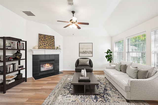 living room featuring ceiling fan, light hardwood / wood-style floors, lofted ceiling, and a tiled fireplace