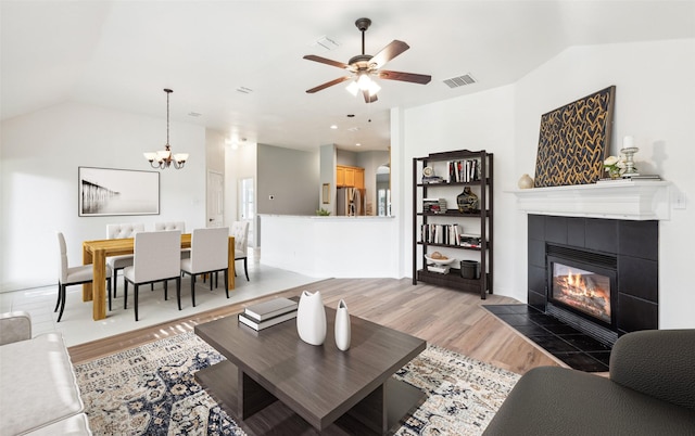 living room with hardwood / wood-style floors, ceiling fan with notable chandelier, vaulted ceiling, and a tiled fireplace