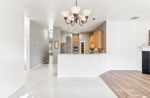 kitchen with appliances with stainless steel finishes, tasteful backsplash, light brown cabinets, a notable chandelier, and a fireplace