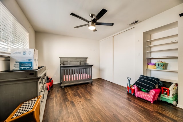 bedroom featuring a crib, a closet, ceiling fan, and dark wood-type flooring