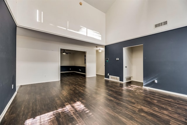 empty room with ceiling fan, dark hardwood / wood-style flooring, and a towering ceiling