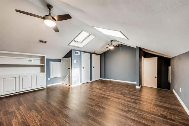 additional living space with built in shelves, dark hardwood / wood-style floors, lofted ceiling with skylight, and ceiling fan