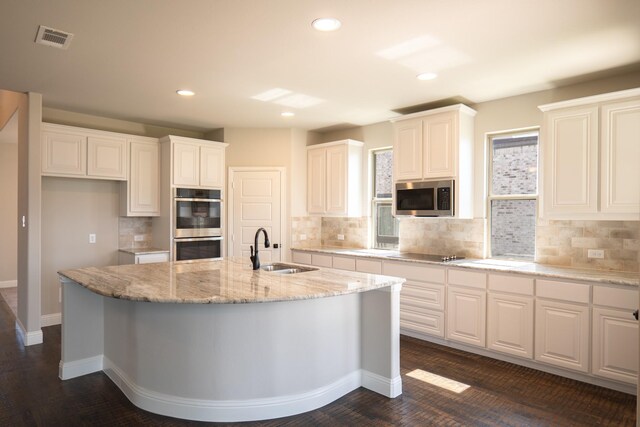 kitchen featuring light stone countertops, appliances with stainless steel finishes, sink, a center island with sink, and white cabinets