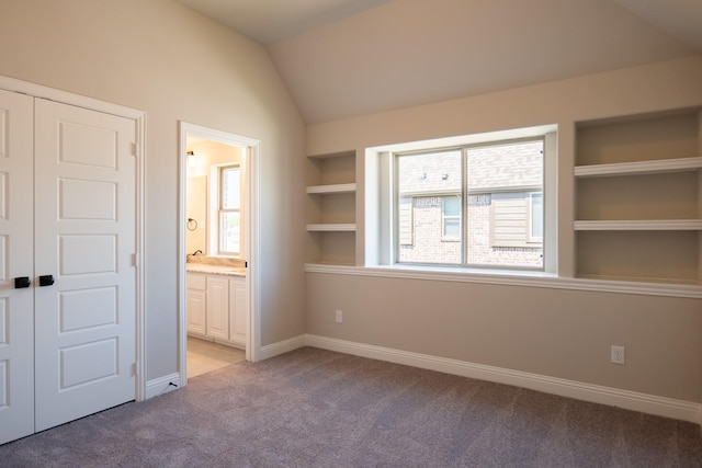 unfurnished bedroom featuring a closet, connected bathroom, vaulted ceiling, and light carpet