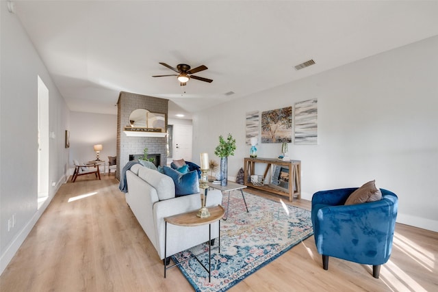 living room featuring ceiling fan, light hardwood / wood-style floors, and a brick fireplace