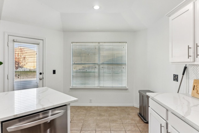 kitchen featuring stainless steel dishwasher, decorative backsplash, light stone countertops, light tile patterned flooring, and white cabinetry