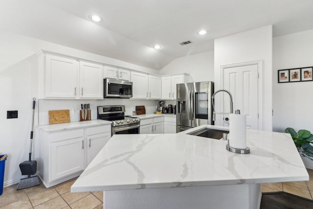 kitchen featuring white cabinets, light stone countertops, appliances with stainless steel finishes, and vaulted ceiling