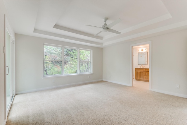 unfurnished bedroom with a raised ceiling, ensuite bath, ceiling fan, and light colored carpet