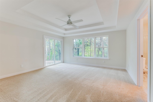 empty room with ceiling fan, a raised ceiling, and light colored carpet