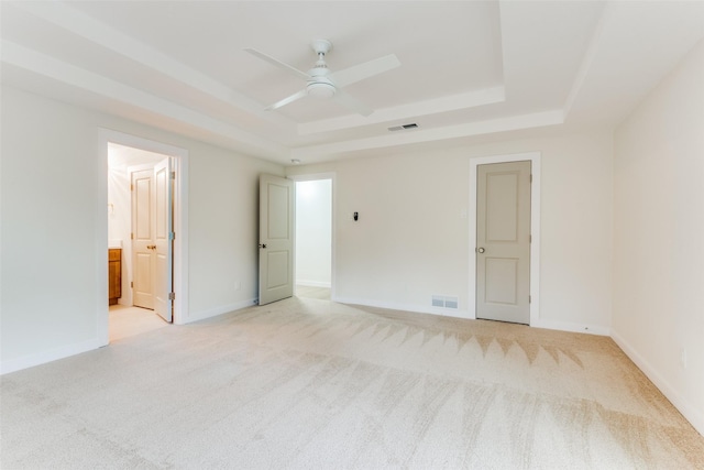 unfurnished bedroom featuring a tray ceiling, ensuite bath, ceiling fan, and light colored carpet