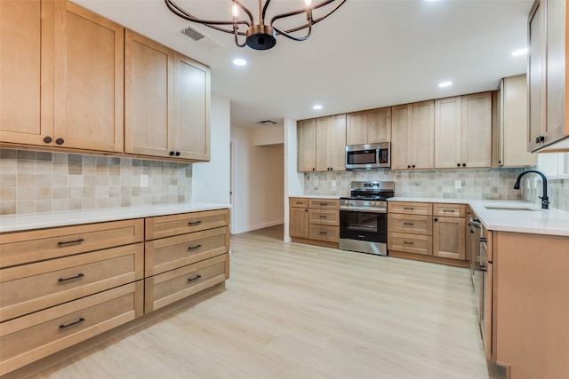 kitchen with sink, decorative backsplash, appliances with stainless steel finishes, light hardwood / wood-style floors, and a chandelier