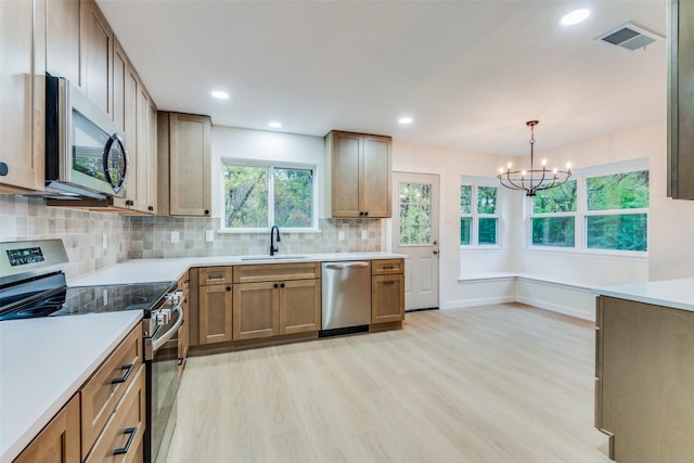 kitchen with appliances with stainless steel finishes, sink, pendant lighting, a chandelier, and light hardwood / wood-style floors