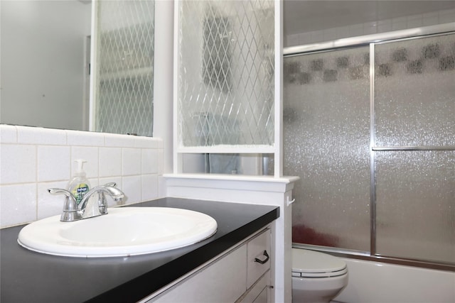 full bathroom with shower / bath combination with glass door, tile walls, vanity, tasteful backsplash, and toilet