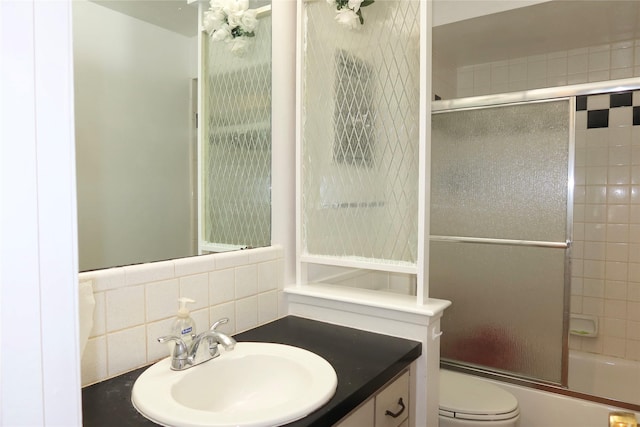 full bathroom featuring shower / bath combination with glass door, decorative backsplash, vanity, and toilet