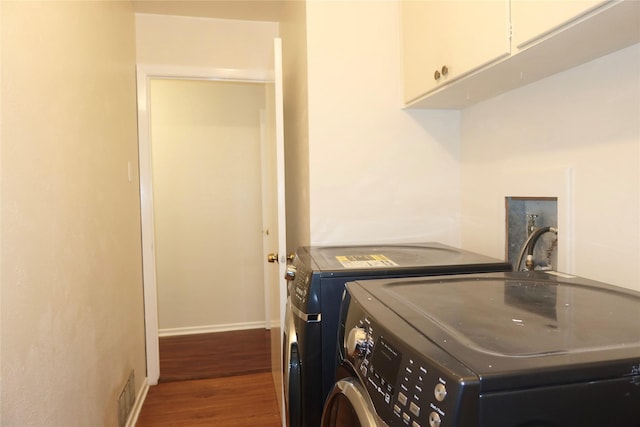 clothes washing area featuring washer and clothes dryer, cabinets, and dark hardwood / wood-style floors