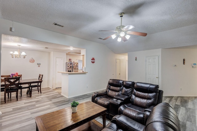 living room with ceiling fan with notable chandelier, lofted ceiling, a textured ceiling, and light hardwood / wood-style flooring