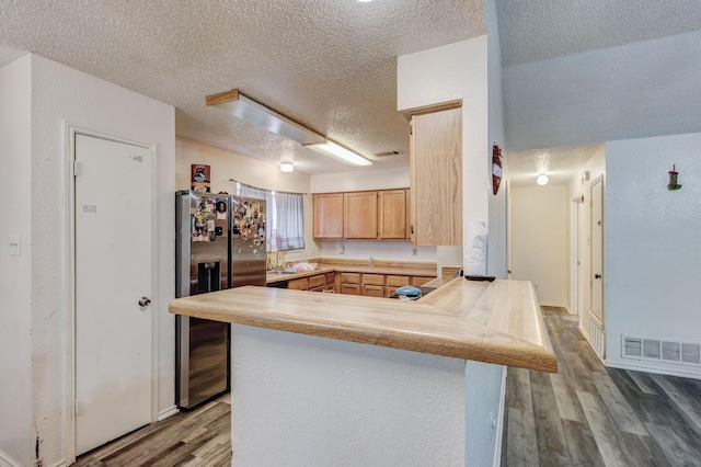 kitchen with kitchen peninsula, stainless steel fridge, hardwood / wood-style floors, a textured ceiling, and light brown cabinetry