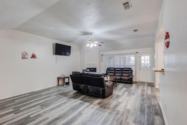 living room with a textured ceiling, ceiling fan, hardwood / wood-style flooring, a fireplace, and lofted ceiling