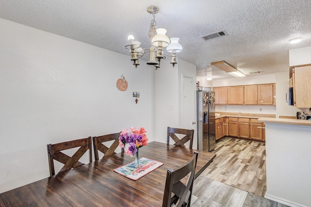 dining area with a notable chandelier, light hardwood / wood-style floors, and a textured ceiling