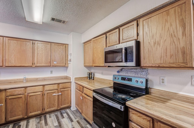 kitchen with a textured ceiling, light wood-type flooring, and stainless steel appliances