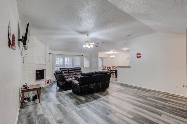 living room featuring a fireplace, wood-type flooring, ceiling fan with notable chandelier, and vaulted ceiling