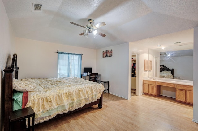 bedroom featuring built in desk, ensuite bath, ceiling fan, light hardwood / wood-style floors, and a textured ceiling