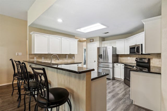 kitchen with a breakfast bar, appliances with stainless steel finishes, kitchen peninsula, hardwood / wood-style floors, and white cabinets