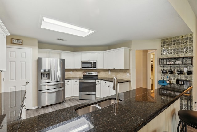 kitchen with backsplash, sink, light hardwood / wood-style floors, white cabinetry, and stainless steel appliances